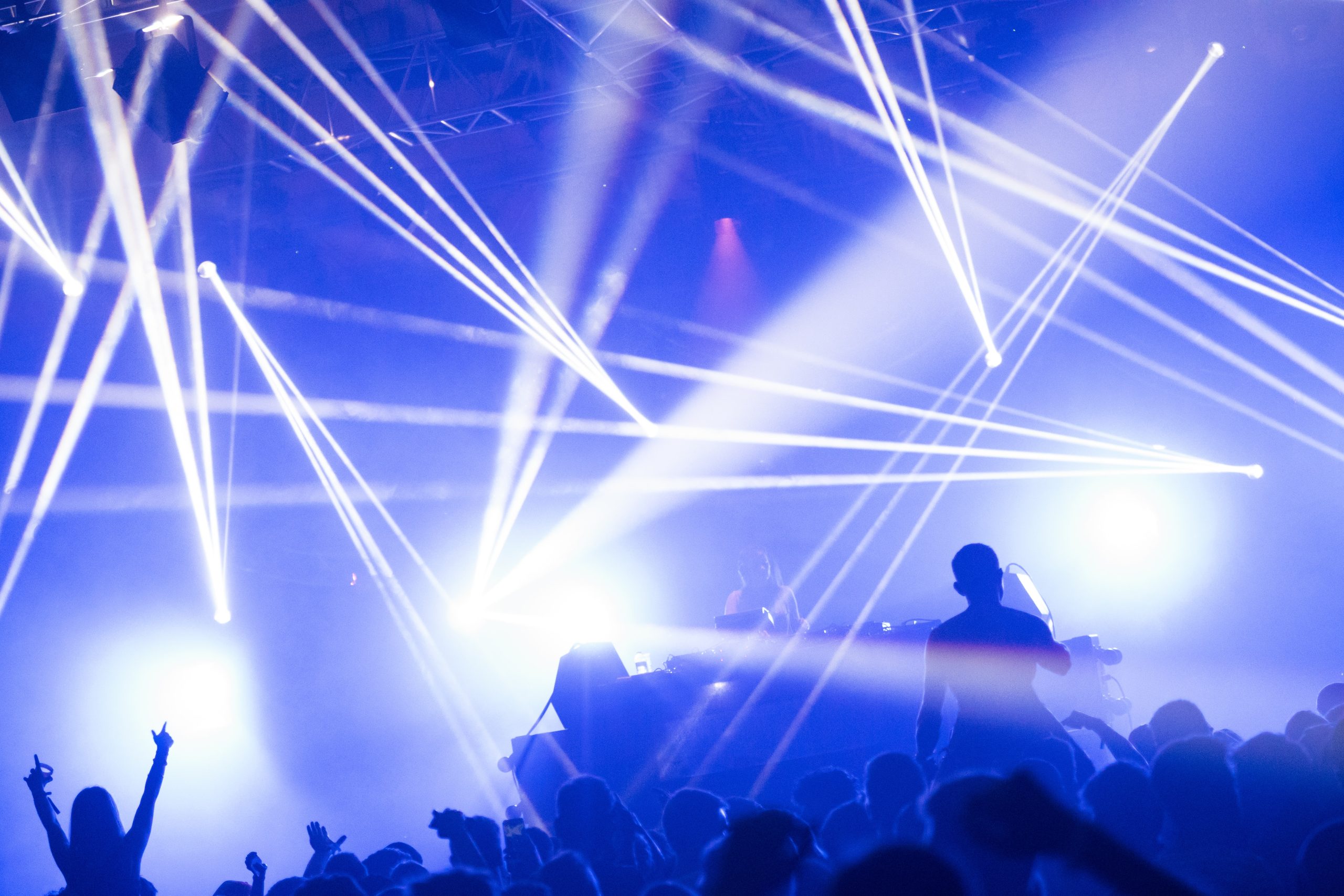 DJ on stage with crowd in front beams of lighting hitting the room create effects