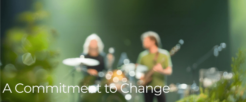 Two musicians perform onstage with blurred greenery and soft lighting. Text reads "A Commitment to Change." Calm, reflective mood.