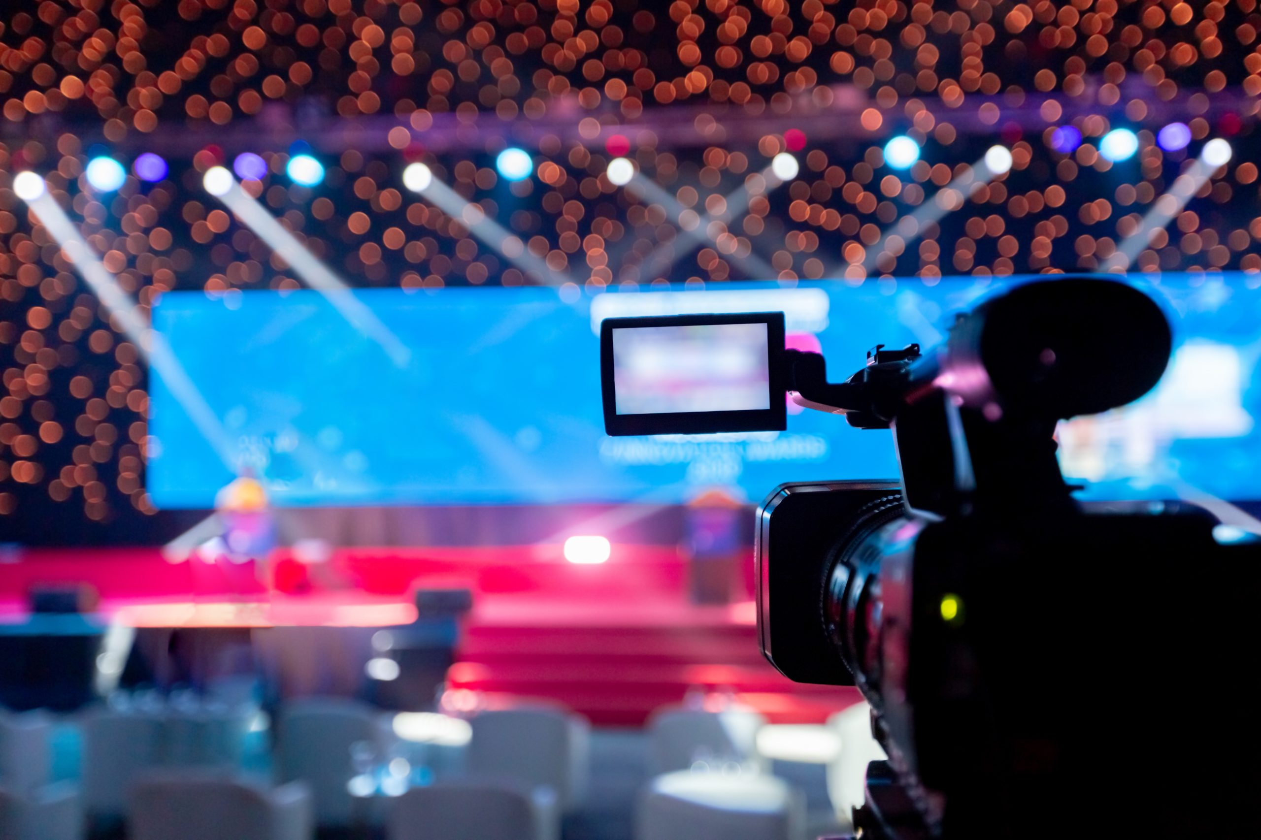 Camera filming an empty stage with colorful lights and blurred bokeh in the background, creating a vibrant and anticipatory mood.